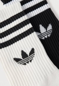Černobílé pruhované ponožky s žebrovanou texturou, na každé ponožce je černé logo. Na manžetě jsou tři horizontální pruhy.
