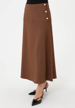 Gonna midi marrone con bottoni perla laterali indossata con decollete slingback nere con punta e top nero su sfondo bianco.