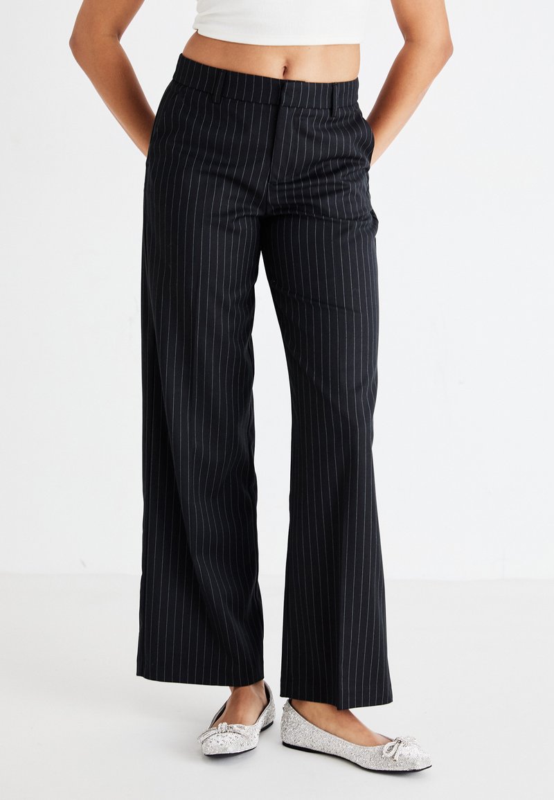 Black pinstriped wide-leg trousers with a smooth texture, featuring a waistband and side pockets. Paired with silver flat shoes.