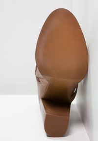 Hnědá podrážka kožené boty obdélníkového tvaru s texturovaným povrchem a výraznými rýhami pro lepší přilnavost. Plochý design paty pro stabilitu.