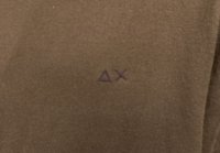 Brauner Stoff mit einem gestickten lila Logo, das ein Dreieck und ein "X" in der unteren Mitte zeigt, glatte Textur, minimalistisches Design.