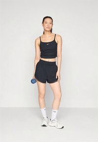 Top cropped atlético preto e calções, com logótipo Nike. Modelo segura um haltere azul, vestindo meias brancas e ténis. Design simples e desportivo.