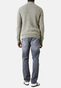 Gebreide trui in lichtgrijs met een hoge kraag, gecombineerd met vervaagde blauwe jeans. De trui heeft een gestructureerd patroon en ribgebreide manchetten.