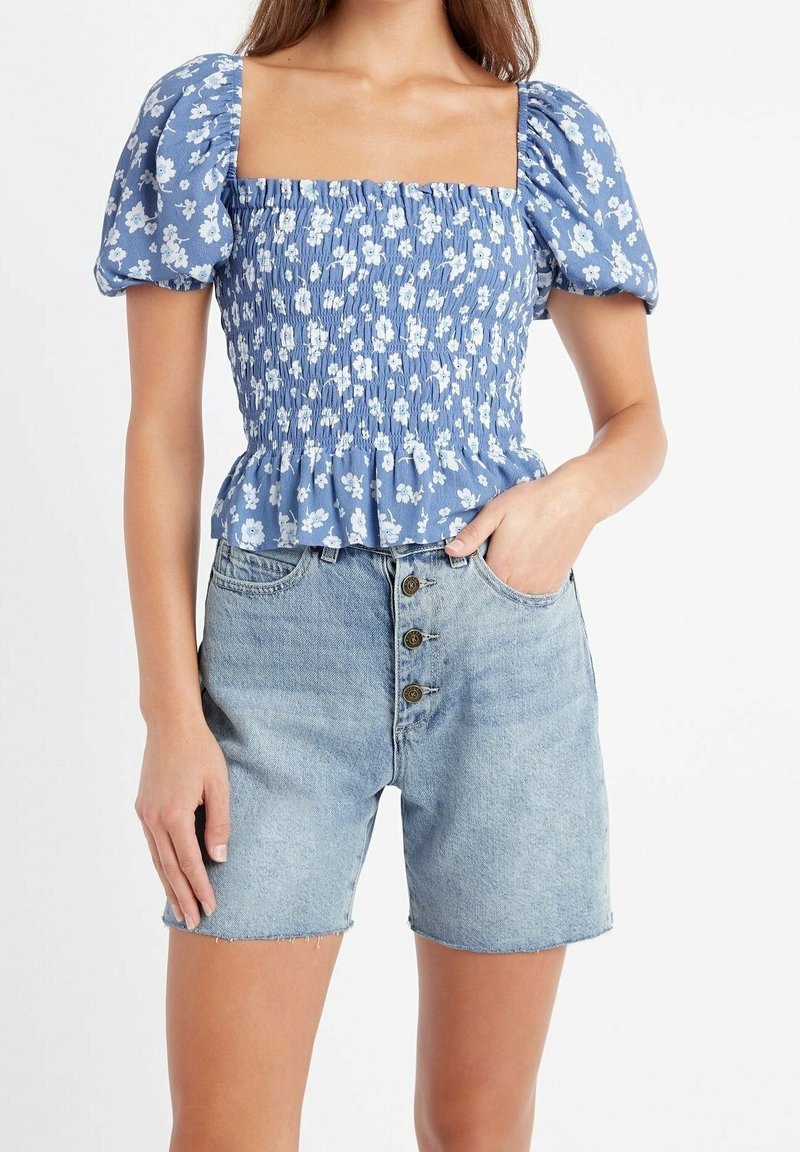 Haut à manches bouffantes floral bleu avec un design smocké et une taille évasée, associé à un short en denim clair taille haute avec un bouton à l'avant.