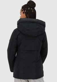 Giacca a vento nera con cappuccio grande, texture liscia e design leggermente svasato, con un emblema posteriore più lungo e dettagli minimi.