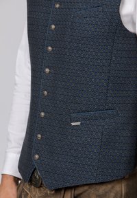 Wollweste mit einem blau-schwarzen geometrischen Muster, ausgestattet mit silbernen Knöpfen und einer Brusttasche mit kontrastierendem Paspel.