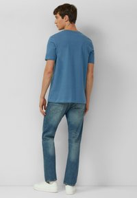 Hellblaues Baumwoll-T-Shirt mit kurzen Ärmeln und Rundhalsausschnitt, kombiniert mit ausgewaschenen blauen Jeans und weißen Turnschuhen. Schlichte, legere Passform.