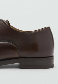 Scarpa in pelle marrone con finitura liscia, punta arrotondata e tacco basso e strutturato. La vista laterale mette in evidenza i dettagli delle cuciture e il design elegante.