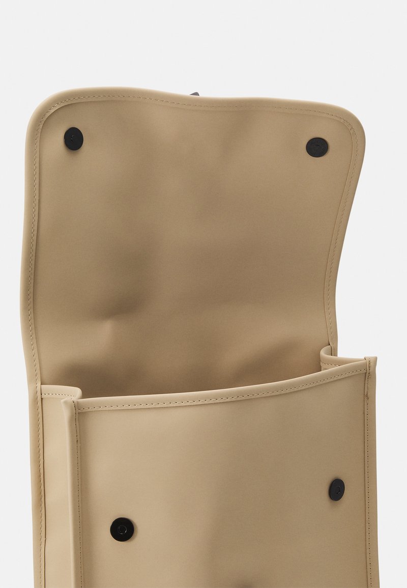 Sac plié tan en matériau lisse, doté de fermetures à bouton noir et d'un intérieur spacieux. Design minimaliste avec des lignes épurées.