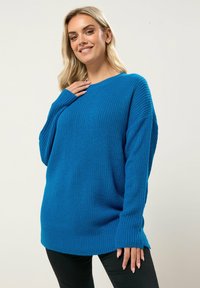 Pull en tricot bleu vif, avec une coupe ample, un col rond et des manches longues avec une texture côtelée et des accents aux poignets.