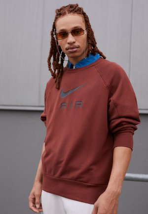 Mørkebrun fleece sweatshirt med grå Nike-logo og "AIR" tekst, med lange ærmer og rund hals, parret med solbriller.