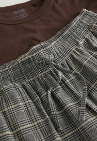 Brown cotton T-shirt layered over black and white plaid pajama shorts with an elastic waistband and drawstring. Smooth texture, casual design.