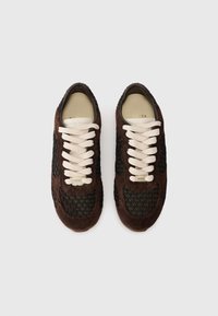 Sneaker in suede marrone con lacci crema, caratterizzati da pannelli in rete nera testurizzati. Punta rotonda e soletta imbottita. Dettaglio del logo dorato sulla linguetta.