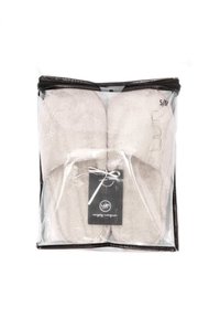 Beiga frottésandaler i genomskinlig plastförpackning, med en svart etikett med ett band, märkt storlek S/M. Mjuk textur, enkelt design.