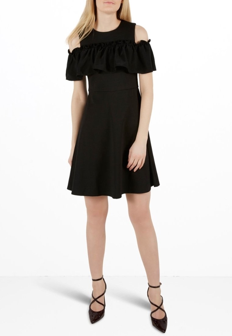 Svart klänning med avskurna rynkade ärmar, figurnära liv, utsvängd kjol och mjuk textur. Kombinerad med spetsiga skor.