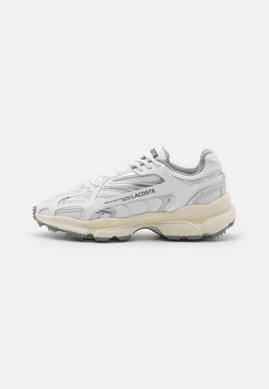 Weißer und grauer Lacoste Sneaker mit Mesh- und synthetischem Obermaterial, dicker beiger Sohle und seitlichem Logo-Schriftzug auf hellem einfarbigem Hintergrund.