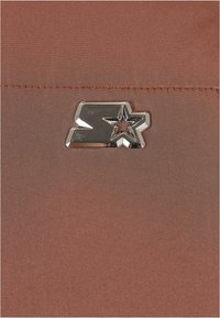 Brązowy materiał o gładkiej fakturze z metalicznym srebrem gwiazda logo. Projekt zawiera subtelne szwy wzdłuż krawędzi.