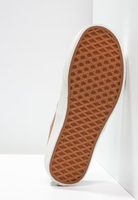 Baskets en daim marron avec accents blancs ; présente une semelle en caoutchouc texturée avec un motif en losanges et un bout arrondi.