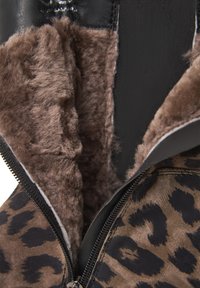 Giacca con stampa leopardata e zip nera, con morbido rivestimento in pelliccia marrone. L'esterno è texturizzato, mescolando tonalità di marrone e nero.