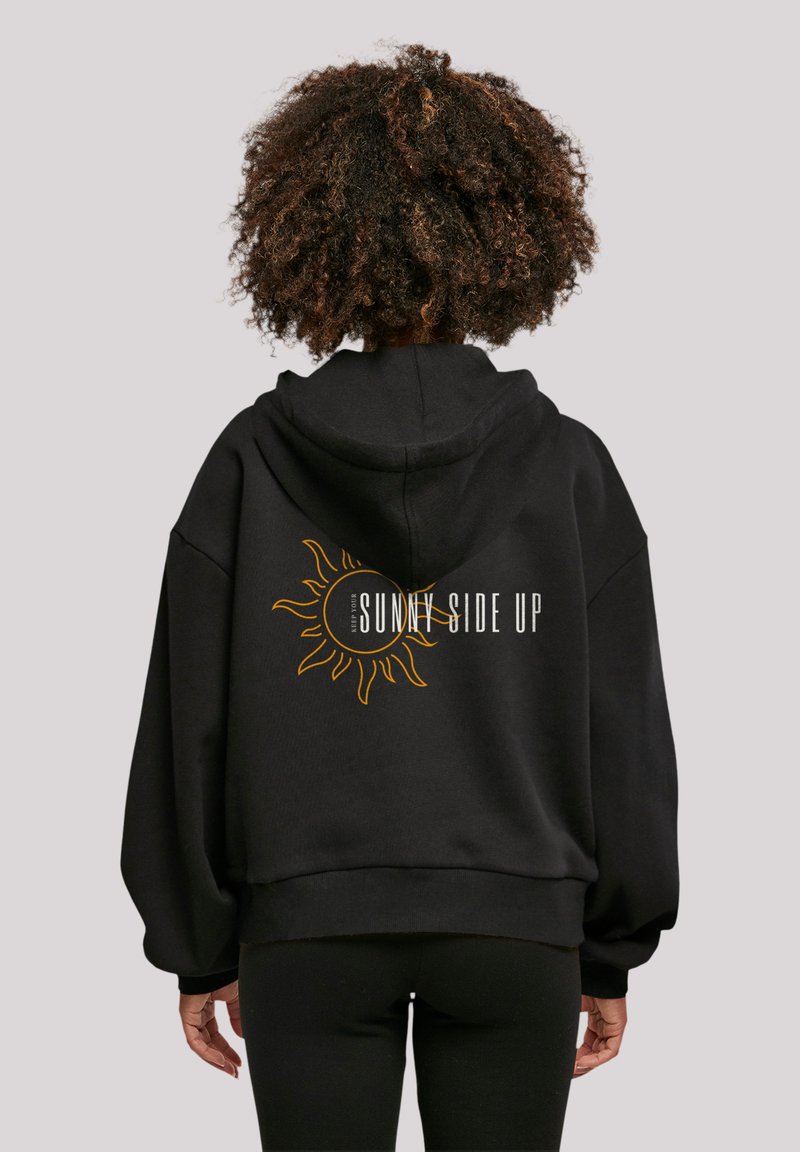 Black oversized hoodie featuring a sun graphic and "SUNNY SIDE UP" text in yellow on the back. Soft material with a relaxed fit.