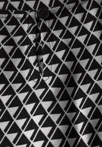 Schwarzer und weißer Stoff mit einem geometrischen dreieckigen Muster, einer Knopfdetaillierung am Ausschnitt und einer strukturierten Oberfläche.