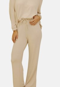 Ensemble de lounge beige en tissu doux, avec une coupe décontractée. Comprend des manches longues, une taille élastique ajustable et une texture lisse. Sans motifs ni accessoires.