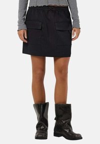 Jupe noire à rayures avec une taille élastique, dotée de deux poches avant. Associée à des bottes noires brillantes jusqu'au genou.