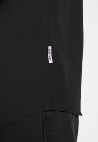 T-shirt in cotone nero con orlo dritto, etichetta laterale con la scritta "ONLY & SONS" e texture liscia senza motivi visibili.