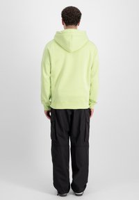 Felpa verde chiaro con cappuccio regolabile, polsini a coste e vita a coste. Abbinata a pantaloni cargo neri con tasche laterali.