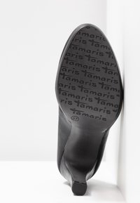 Chaussure à talon haut noire avec une tige en cuir lisse et une semelle en caoutchouc texturé arborant la marque "Tamaris", présentée de profil.