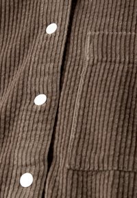 Tela de pana marrón con costillas verticales, que presenta un bolsillo de parche y botones a presión blancos para el cierre. Textura suave.
