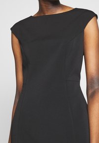 Svart ärmlös klänning med båthalsringning, strukturerad passform och mjukt material; har vinklade sömmar för en skräddarsydd look.