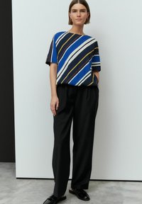 Haut à manches courtes bleu et rayé avec des lignes horizontales, associé à un pantalon noir taille haute et des chaussures noires brillantes.