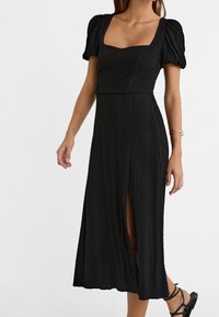 Vestido negro midi con escote cuadrado, mangas cortas abullonadas y una tela texturizada. Presenta una abertura lateral y una cintura ajustada.