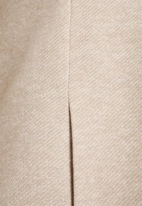 Beige neulottu kangas, jossa on hienovarainen tekstuuri ja diagonaalinen halkiova sauma. Pehmeä, hengittävä materiaali, jossa on yhtenäinen kuvio.