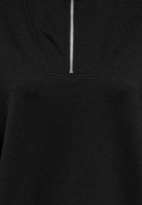 Pull-over noir avec un col zippé au quart, présentant une texture lisse et un détail de couture subtil autour de la zone de la fermeture éclair.