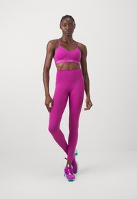 Sujeción deportiva rosa con tirantes ajustables, combinada con leggings rosas de tiro alto. Calzado con acentos en rosa y verde azulado. Tejido suave y elástico.