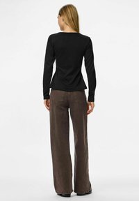 Czarny longsleeve z okrągłym dekoltem, w połączeniu z brązowymi spodniami o szerokich nogawkach z tylnymi kieszeniami i fakturowanym wykończeniem.