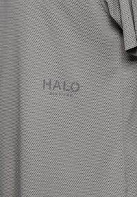 Szary, teksturowany materiał z siatkowym wzorem. Na tkaninie widnieje słowo "HALO" oraz numer modelu wydrukowane w ciemniejszym odcieniu szarości. Minimalistyczny i funkcjonalny styl.