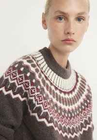 Jersey de punto en lana marrón con un canesú estampado en blanco, rojo y gris, que presenta un cuello acanalado y diseños geométricos.