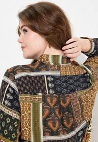 Camisa de manga larga con estampado que presenta una mezcla de elementos en verde oscuro, dorado y naranja, con varios diseños intrincados y un collar clásico.