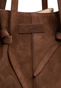 Brązowa torba na ramię z zamszu o gładkiej fakturze, wyposażona w metkę z logo i przeszycia, prezentująca prosty, a zarazem elegancki design.