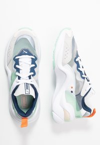 Vita och grå idrottsskor med mesh och syntetiska material, marinblå detaljer, mintgrön sula, orange hälla och en strukturerad design.
