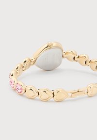 Ρολόι βραχιόλι με συνδέσμους σε σχήμα καρδιάς σε χρυσό τόνο, με ροζ κρύσταλλα και ένα μικρό κρύσταλλο στο κουρδιστήρι, με τη μάρκα Swarovski στη πόρπη και στην πίσω πλευρά της κάσας.