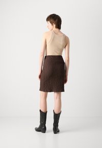 Brun strukturert skjørt med tettsittende midje, kombinert med en beige tanktop og svarte cowboystøvler. Synlig søm og knelengde.