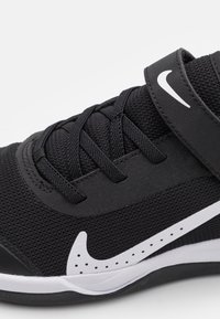 Black athletic shoe with a textured mesh upper, feature laces, adjustable strap, and a white Nike swoosh logo on the side.