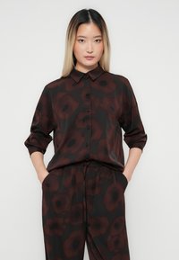 Mørk blomstrete bluse med krage, med store røde og svarte blomster på svart bakgrunn, laget av et glatt, lett stoff.