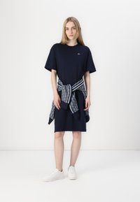 Navy cotton t-shirt dress with short sleeves, relaxed fit. Patterned sweater tied at waist, paired with white sneakers.