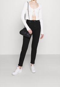 Top blanco de manga larga acanalado con un corte y detalles de cordones, combinado con jeans ajustados negros y zapatillas blancas. Incluye un bolso negro texturizado.
