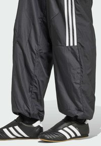 Svarta, lätta träningsbyxor med löst snitt, med tre vita ränder på sidan. Tillsammans med svarta och vita fotbollsskor.